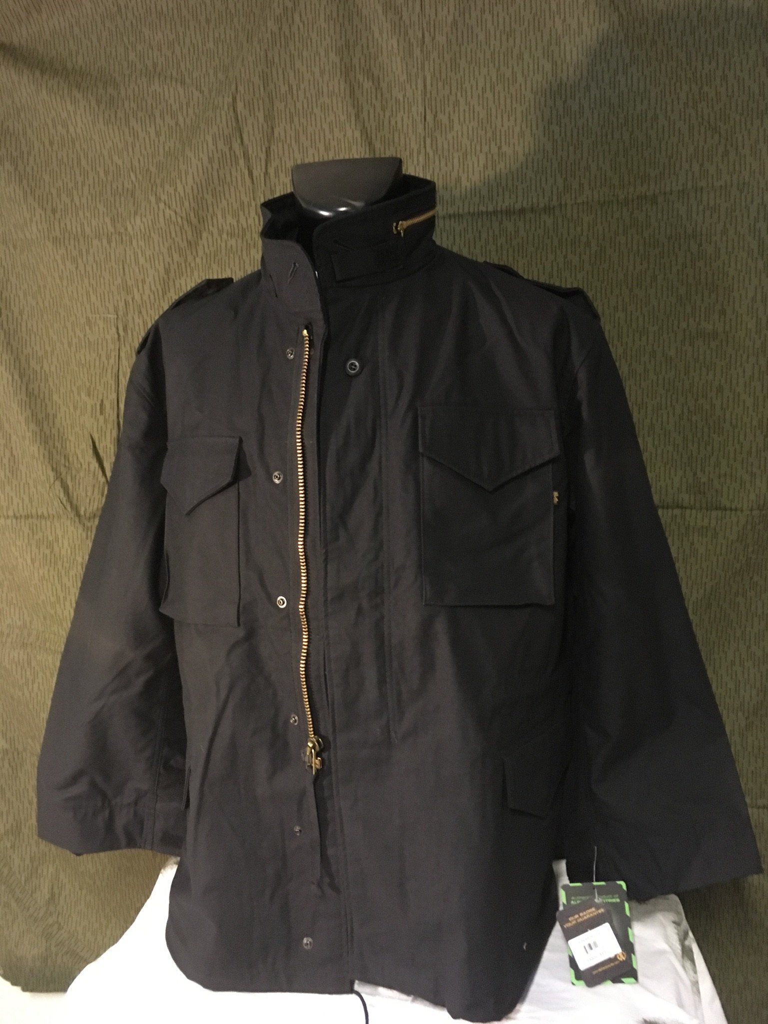 Schwarze M-65-Feldjacke mit Reißverschluss und mehreren Taschen an einer Schaufensterpuppe.