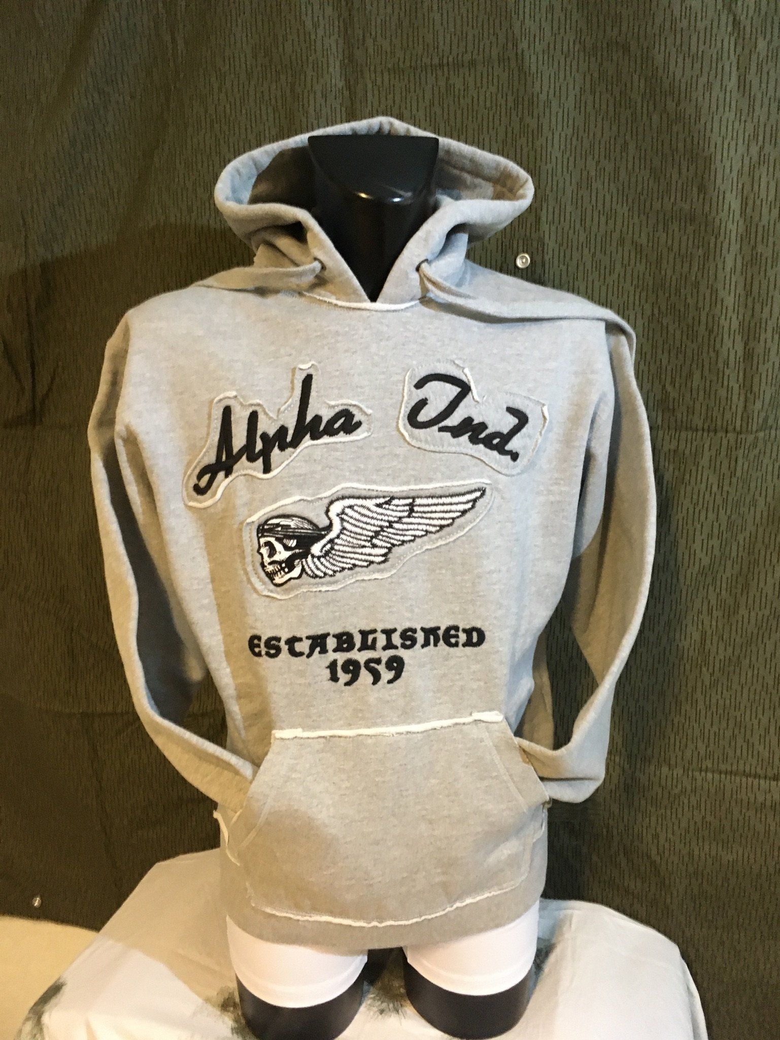Grauer Kapuzenpullover mit „Alpha Ond“-Text und Logo auf einer Schaufensterpuppe.