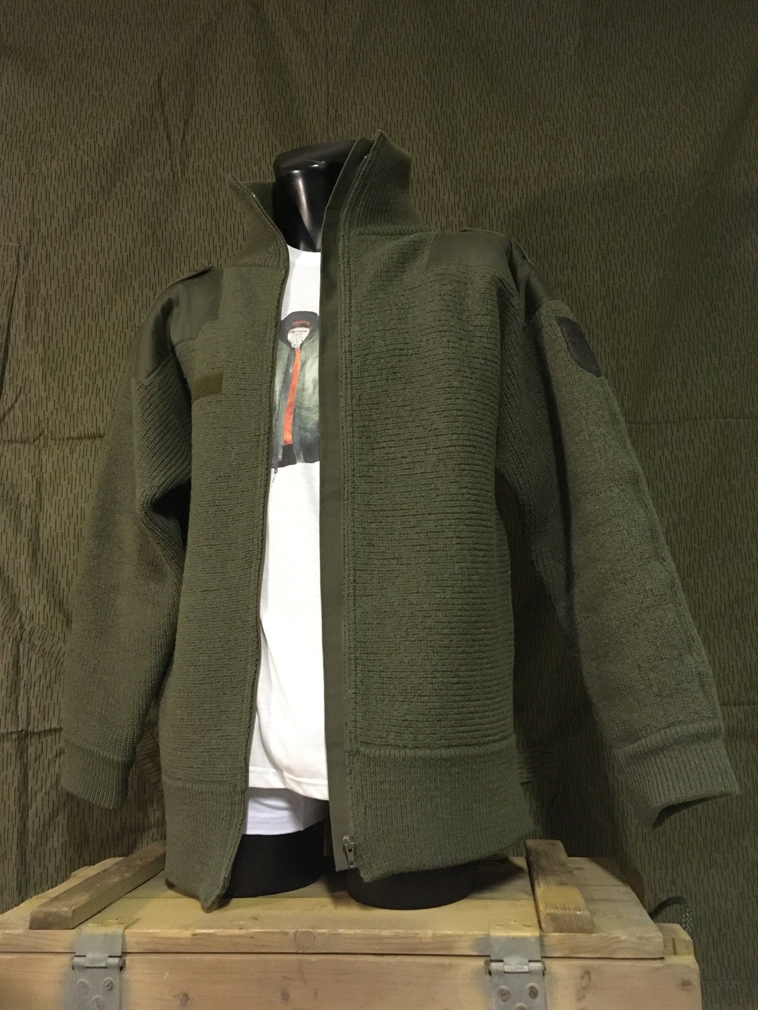 Grüne Steppjacke auf einer Schaufensterpuppe, über einem weißen Hemd. Auf einer Holzkiste platziert.