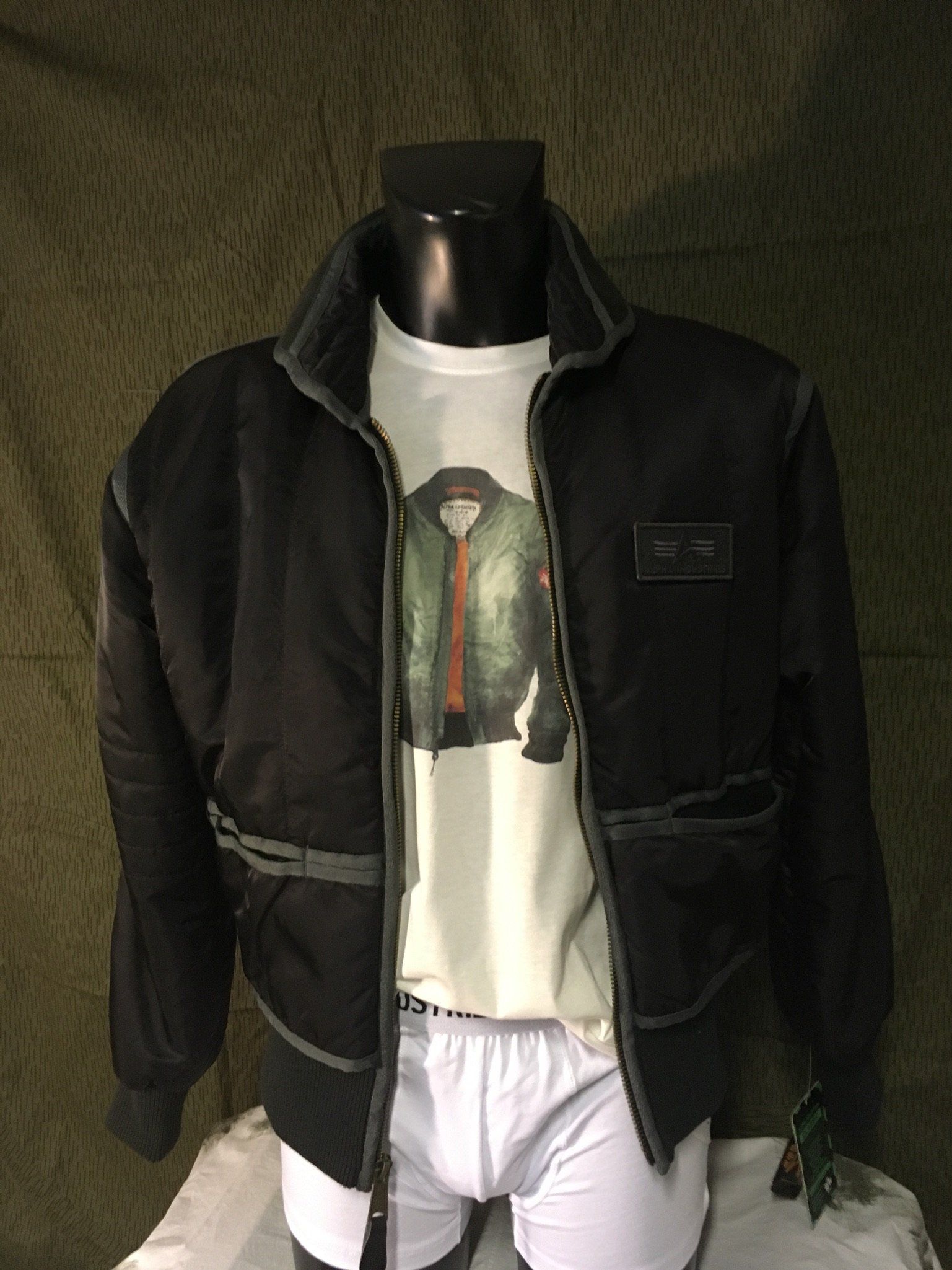 Schwarze Jacke über weißem T-Shirt und Unterwäsche auf einer Schaufensterpuppe.