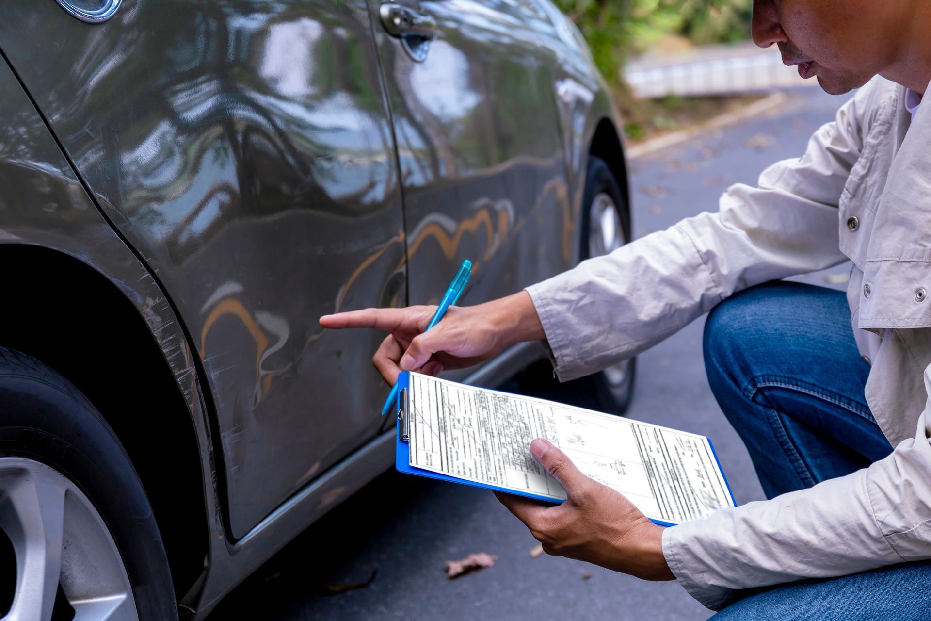 Person noting damage on a car door with clipboard and pointing at a dent. Person noting damage on a car door with clipboard and pointing at a dent.