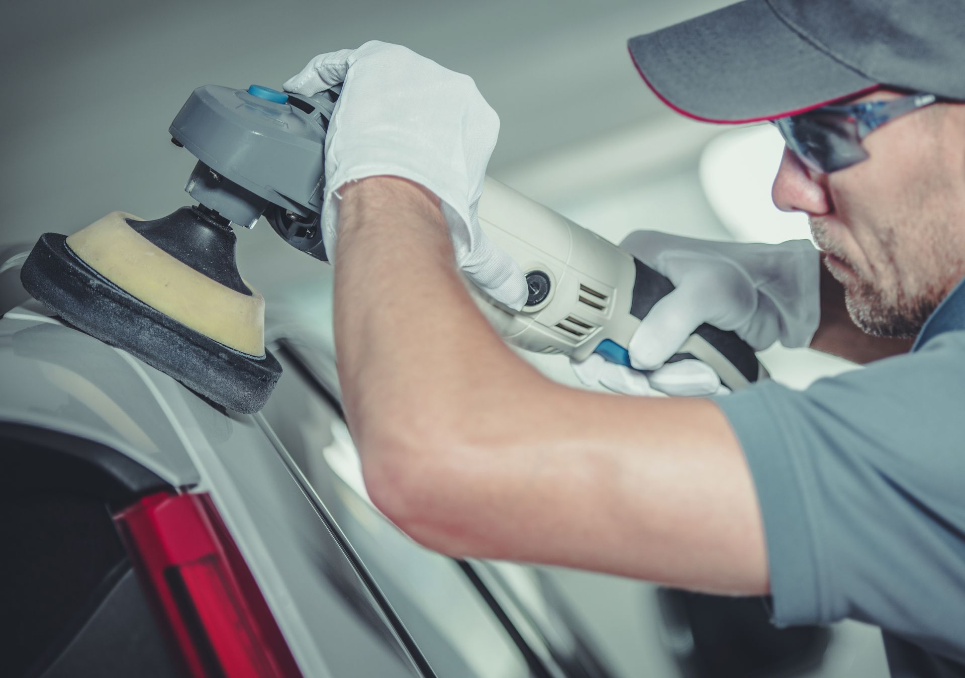 A male collision center worker polishes the exterior of a white car. A male collision center worker polishes the exterior of a white car.