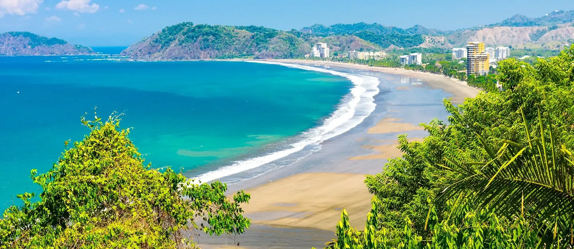 Tropical beach with turquoise water, sandy shore, and green hills under a clear blue sky