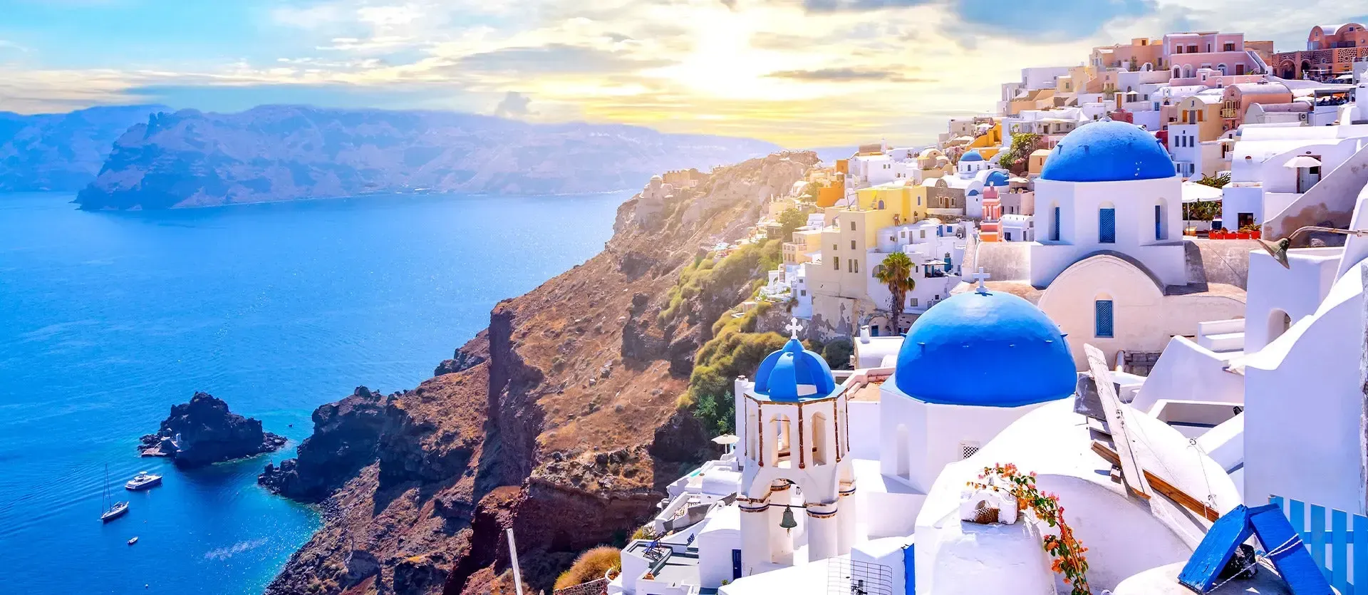 White-blue domed buildings on a cliff overlooking a bright blue sea at sunset in Santorini