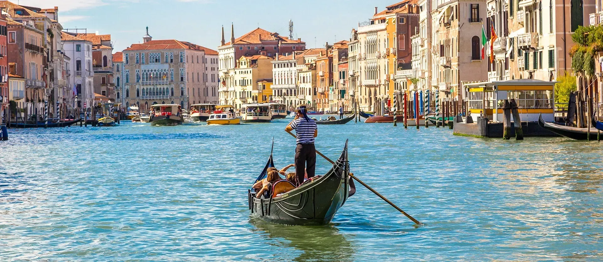 Gondola on a bright blue Venetian canal lined with colorful buildings and boats