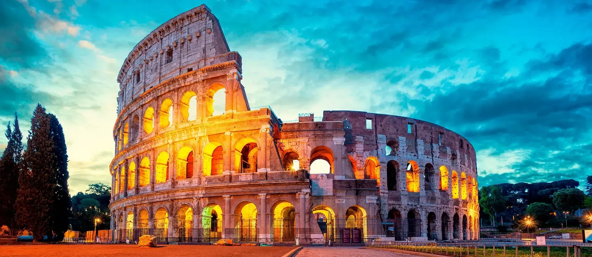 The illuminated Colosseum in Rome at dusk under a blue sky.