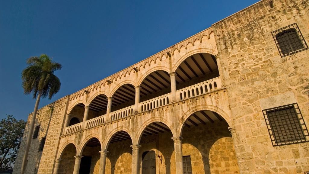 Sunlit stone building with arched balconies and barred windows against a blue sky