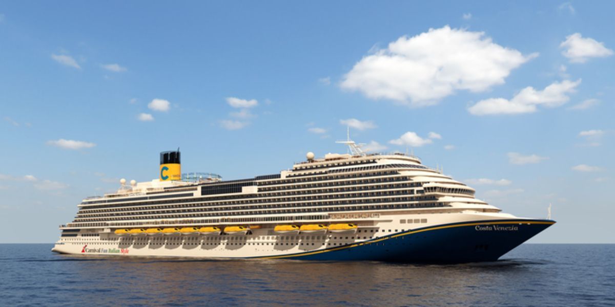 A large cruise ship sails on calm blue water under a partly cloudy sky.