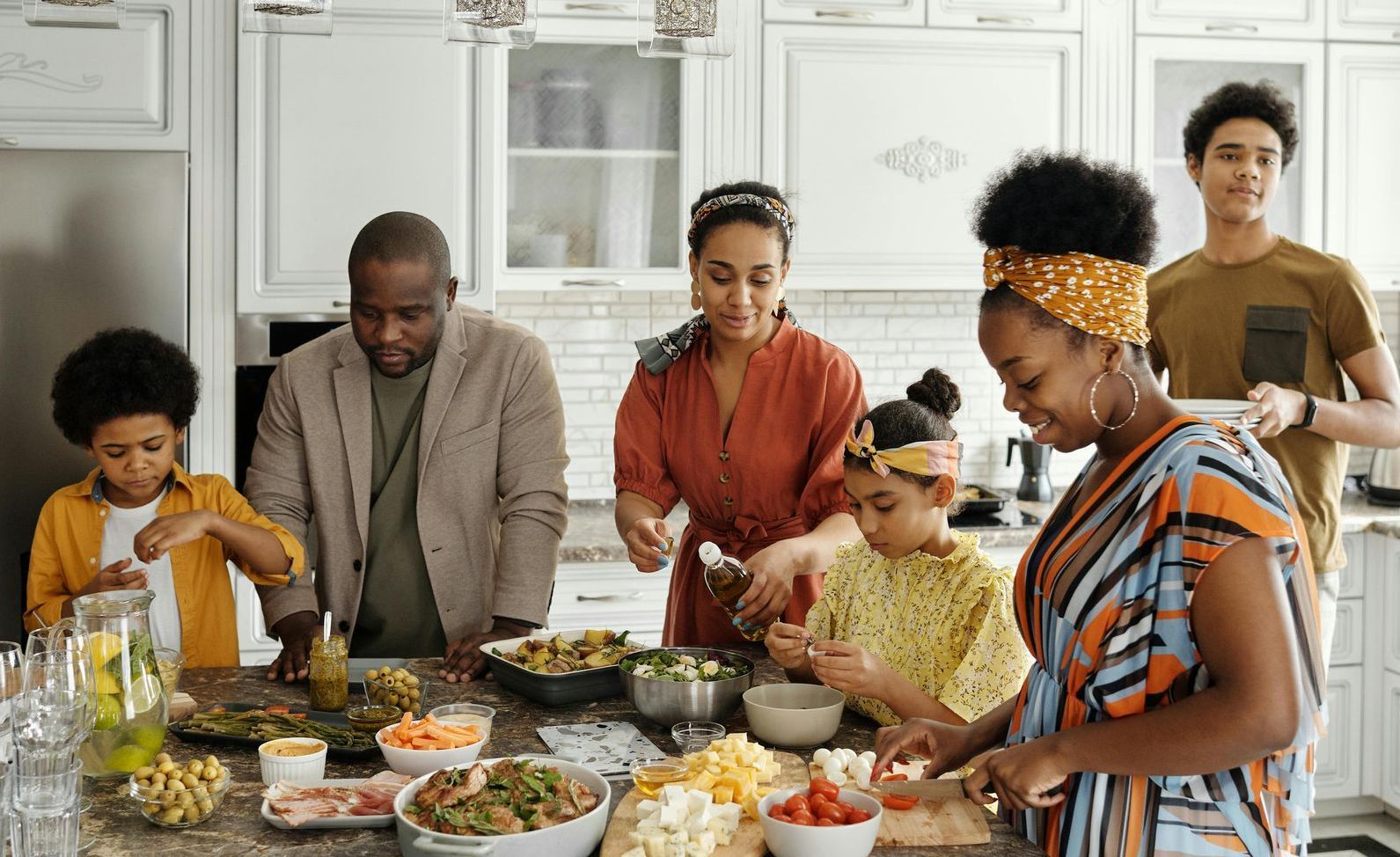 Family preparing a meal together in a bright kitchen with dishes and ingredients on the counter.
