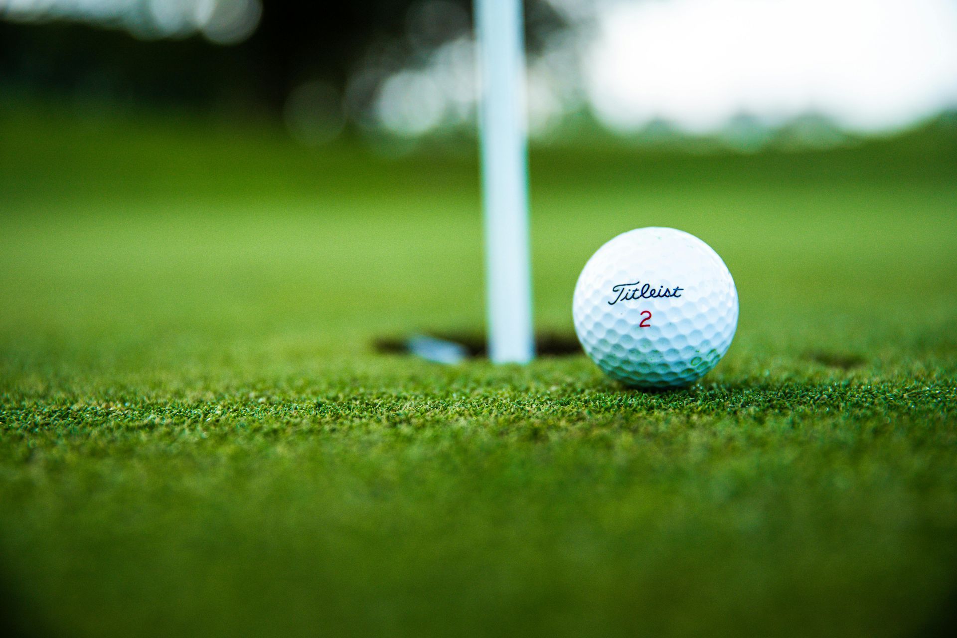 Golf ball near the hole on green grass with a flag in the background.