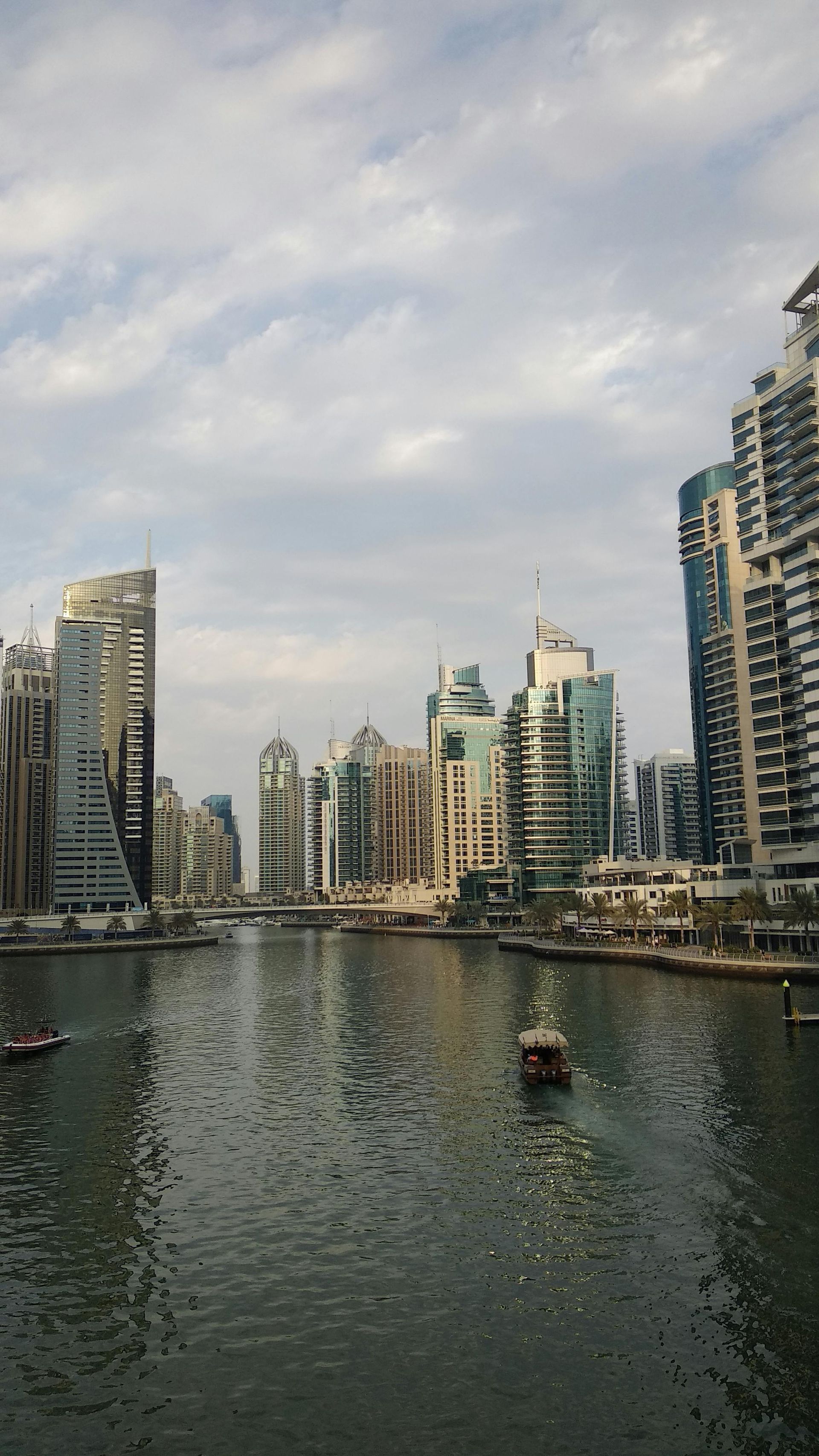 Waterway lined with modern skyscrapers, small boats, overcast sky.