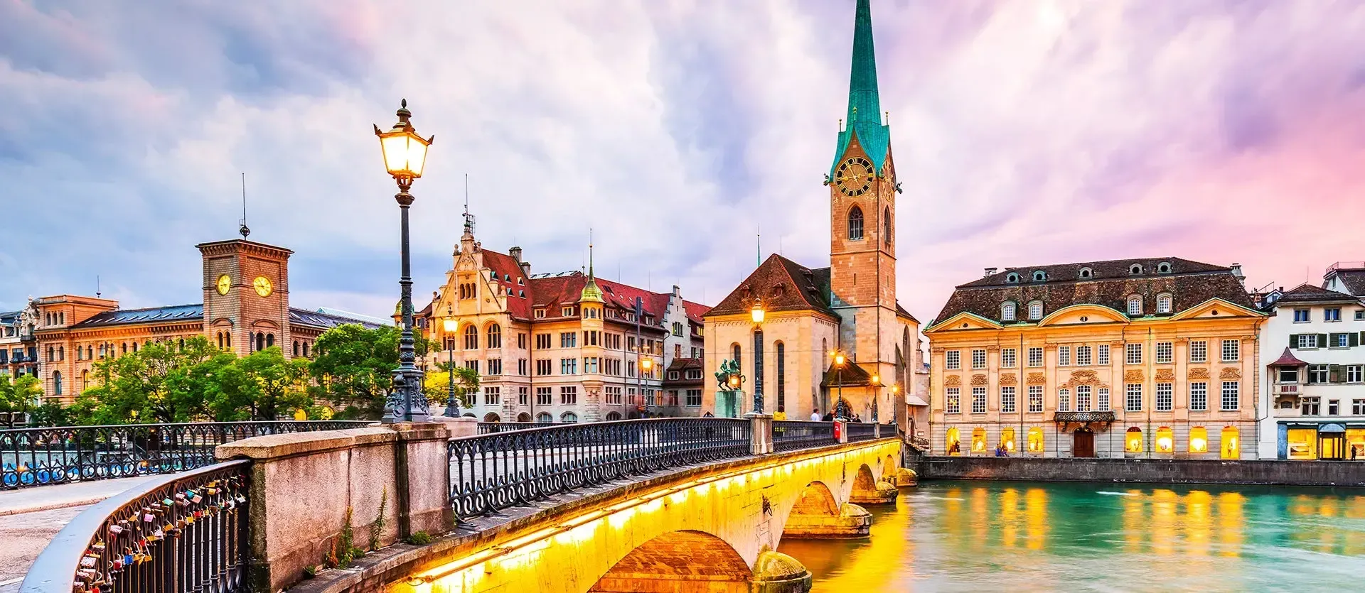 Colorful riverside city at sunset with a lit bridge and historic buildings beside the water