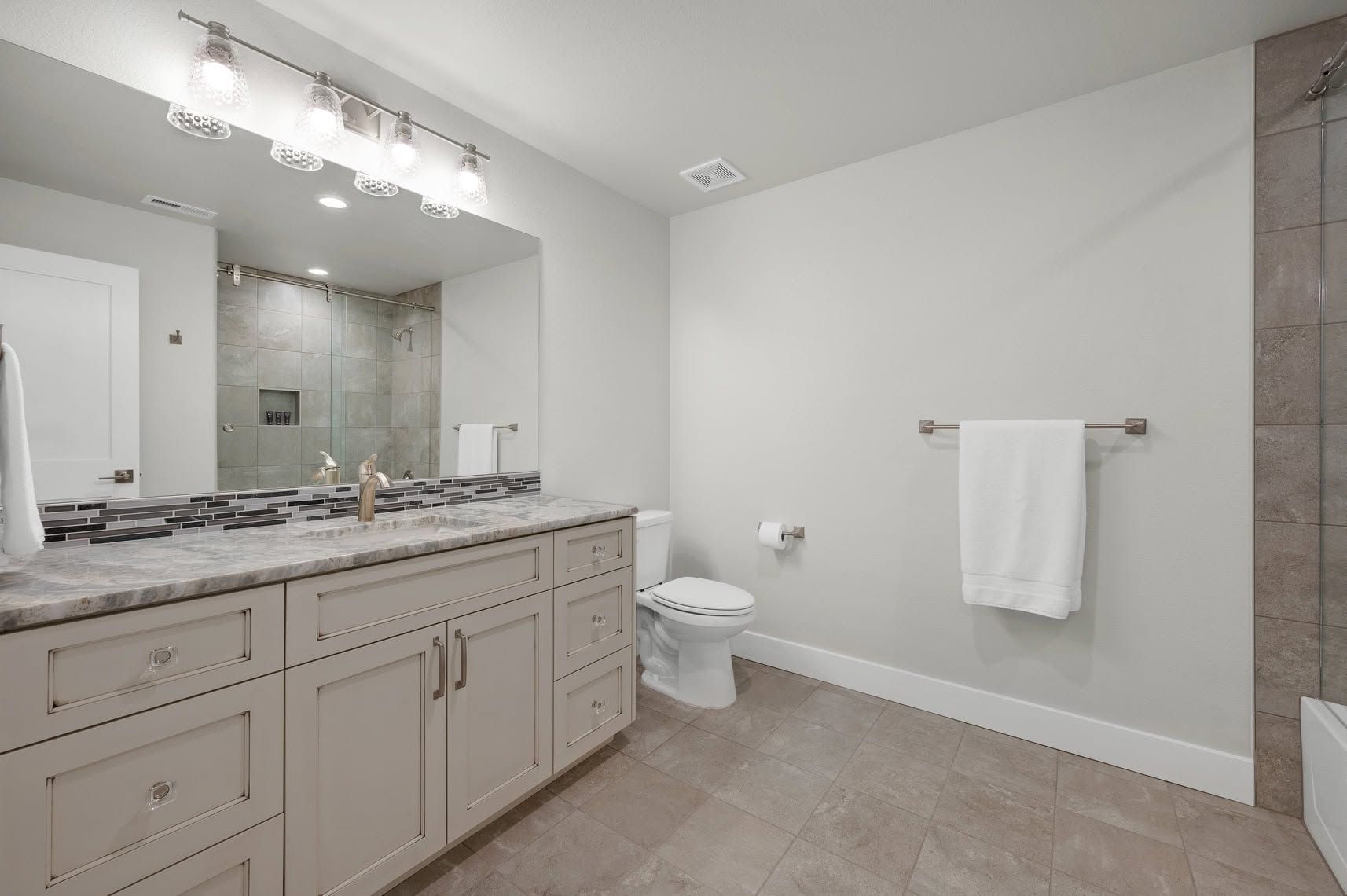 Bright beige bathroom with double sinks, large mirrors, vanity cabinets, and a chandelier.