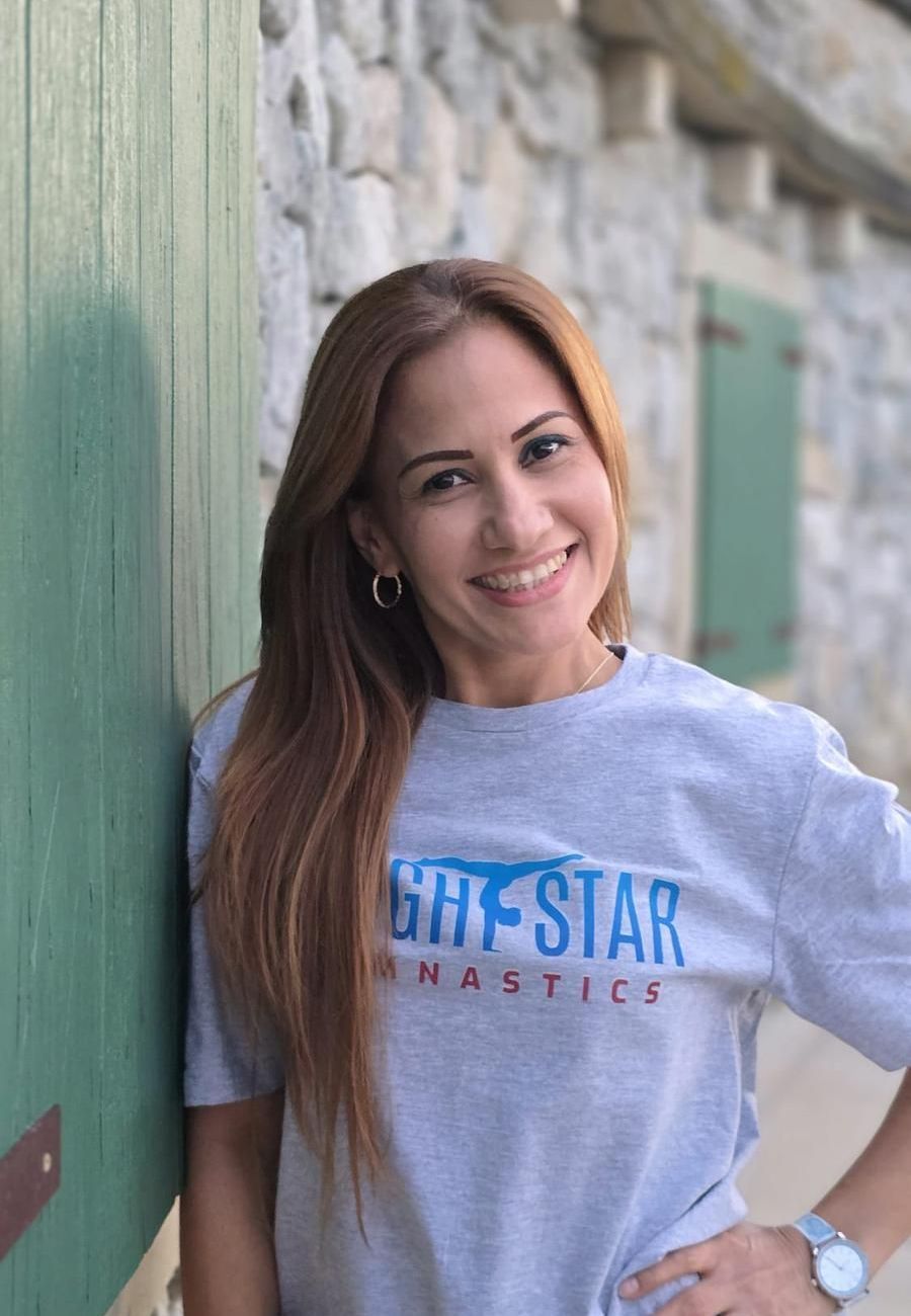 A woman wearing a gray t-shirt is smiling and leaning against a stone wall.