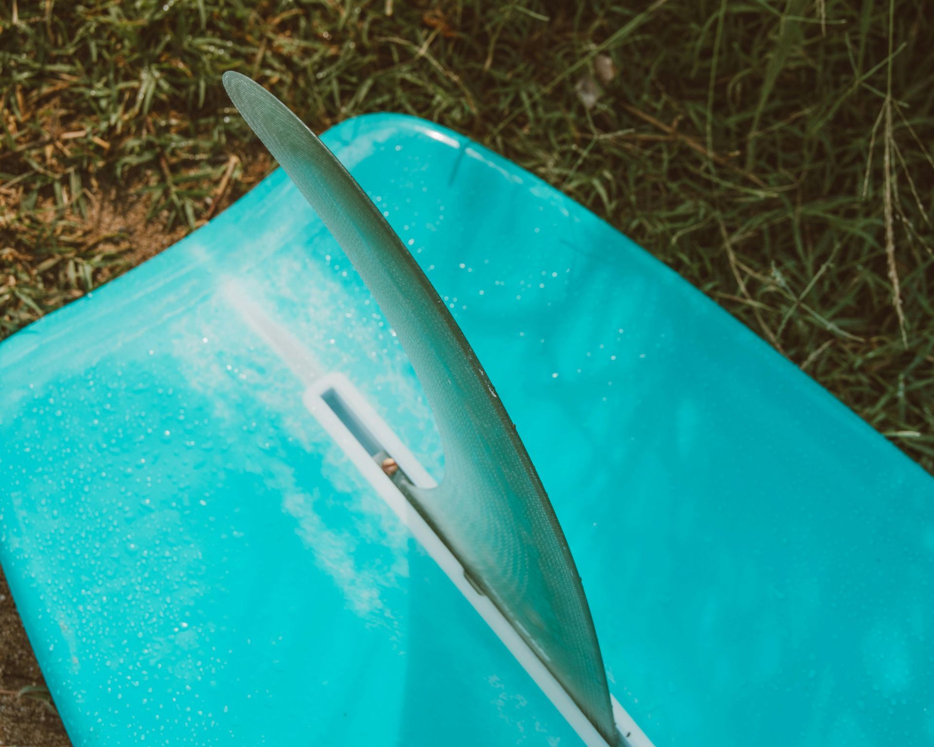 A blue surfboard with a white fin is laying on the grass.