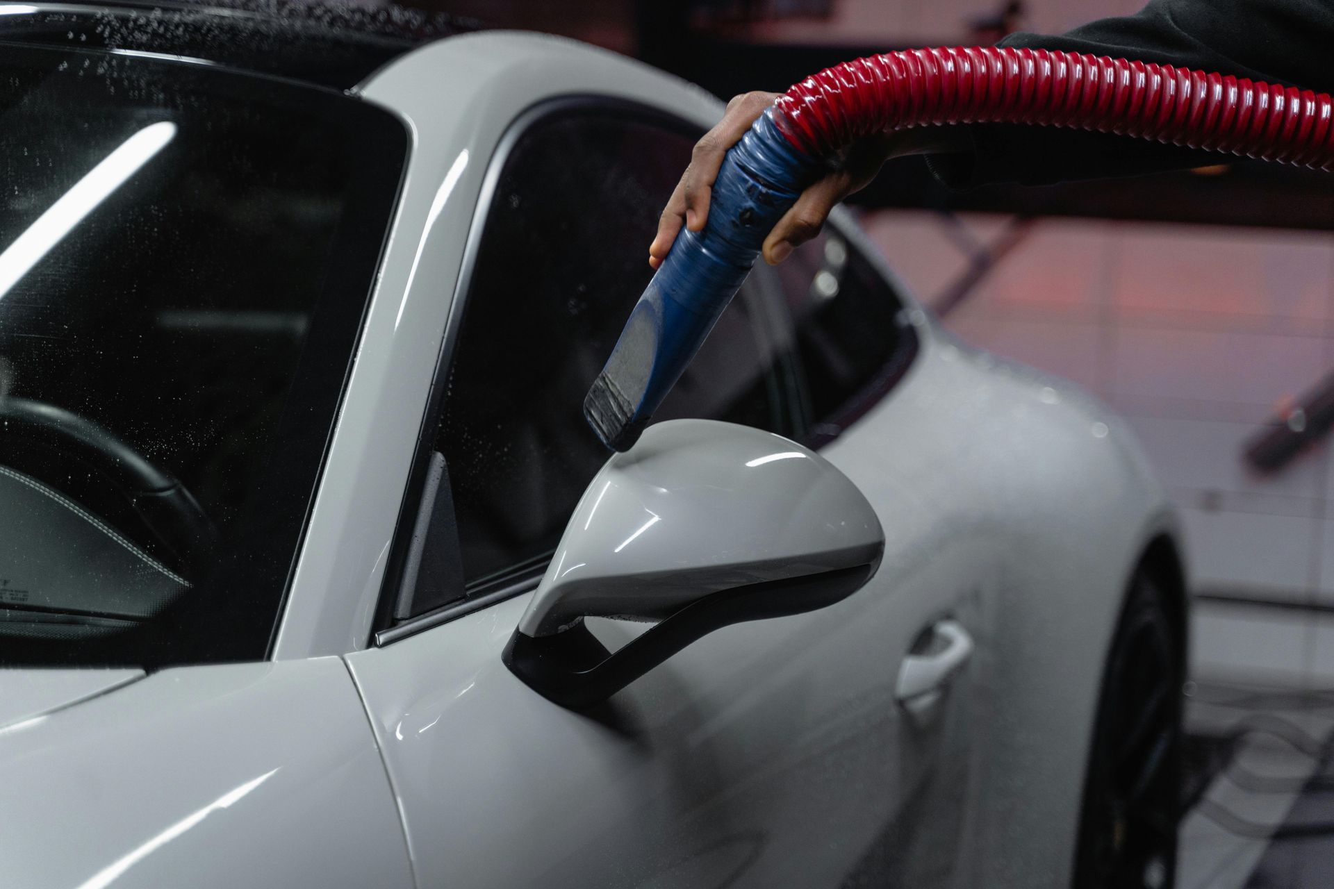 A person is cleaning a white car with a vacuum cleaner