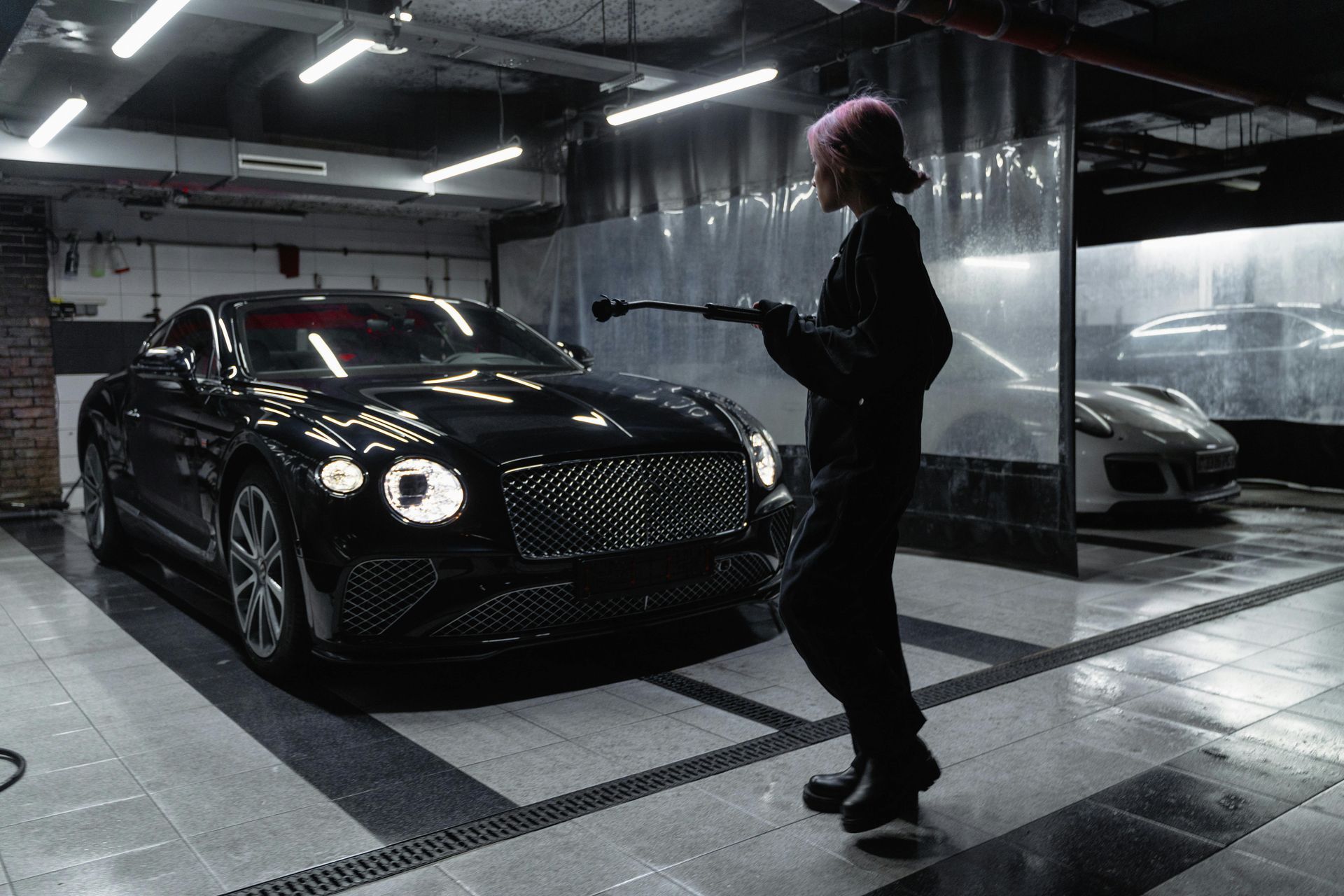 A woman is washing a black bentley in a garage.