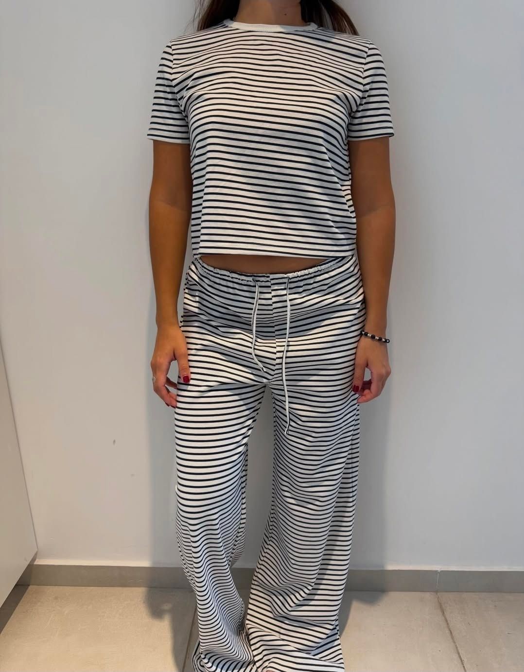 Persona de pie contra una pared, con un top corto de rayas blancas y negras y pantalones a juego.