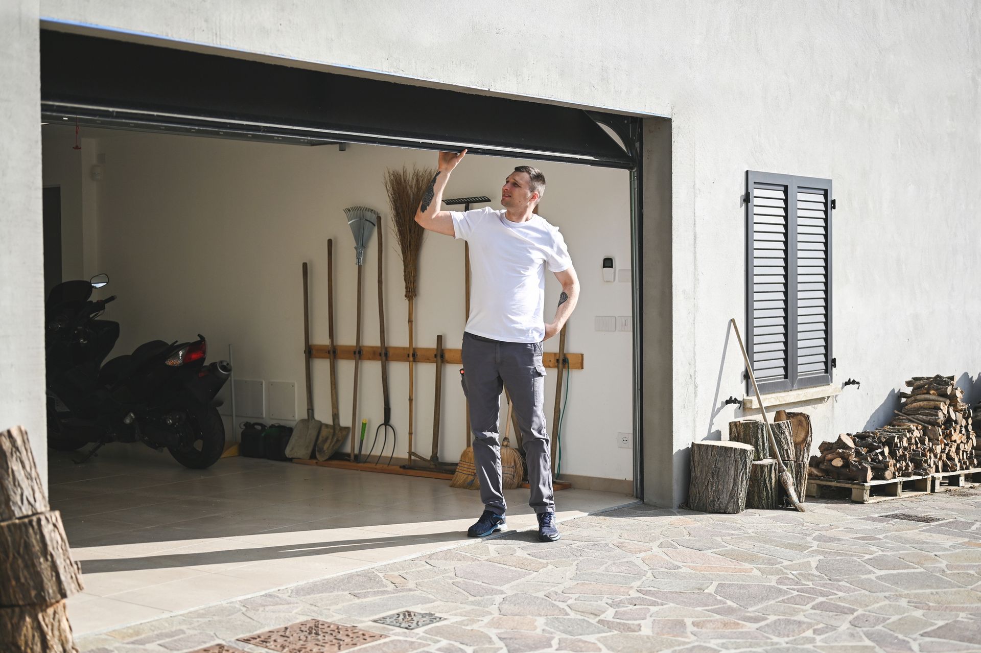 Person standing in front of an open garage with tools and a motorcycle inside.