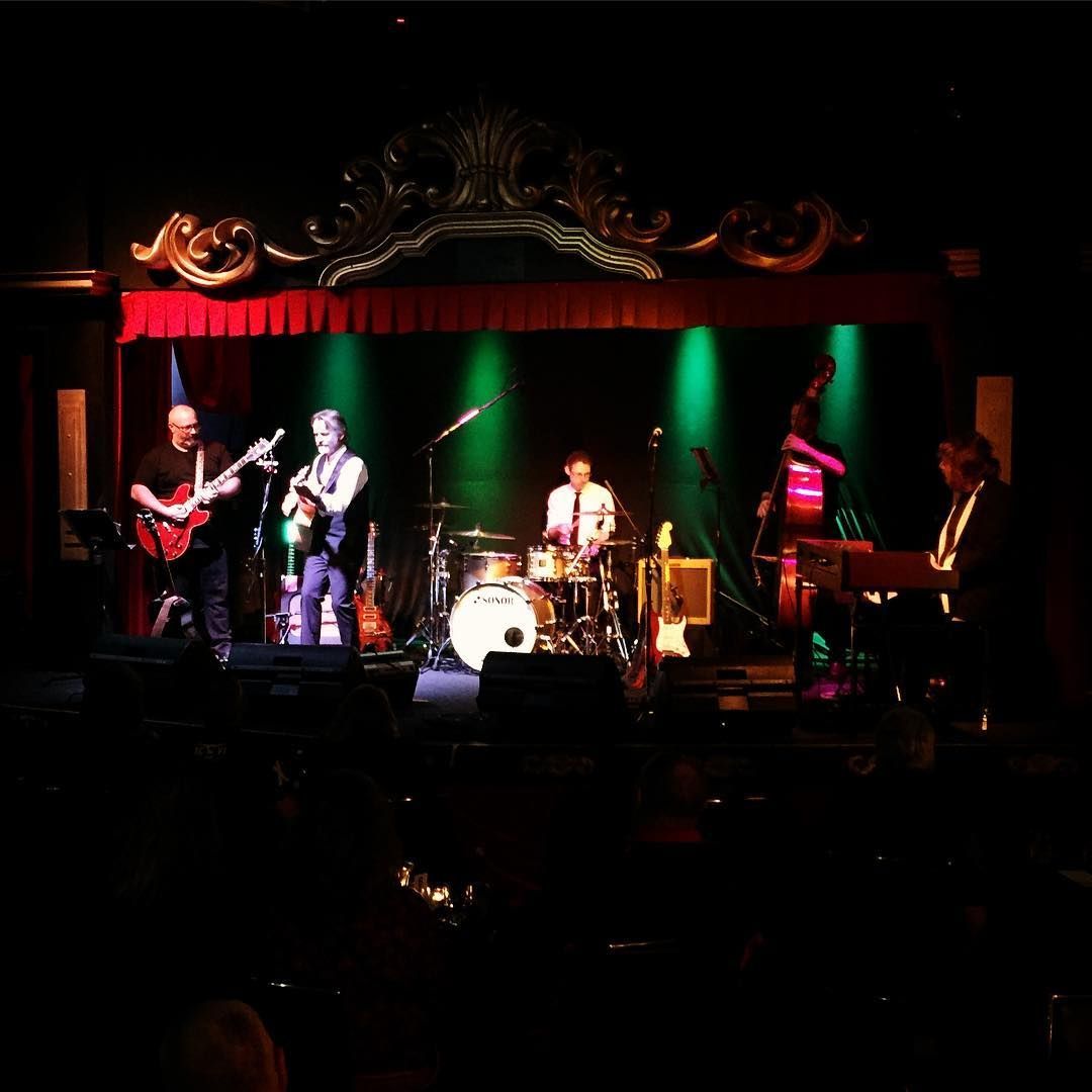 Live band performing on a dark stage with red and green lights