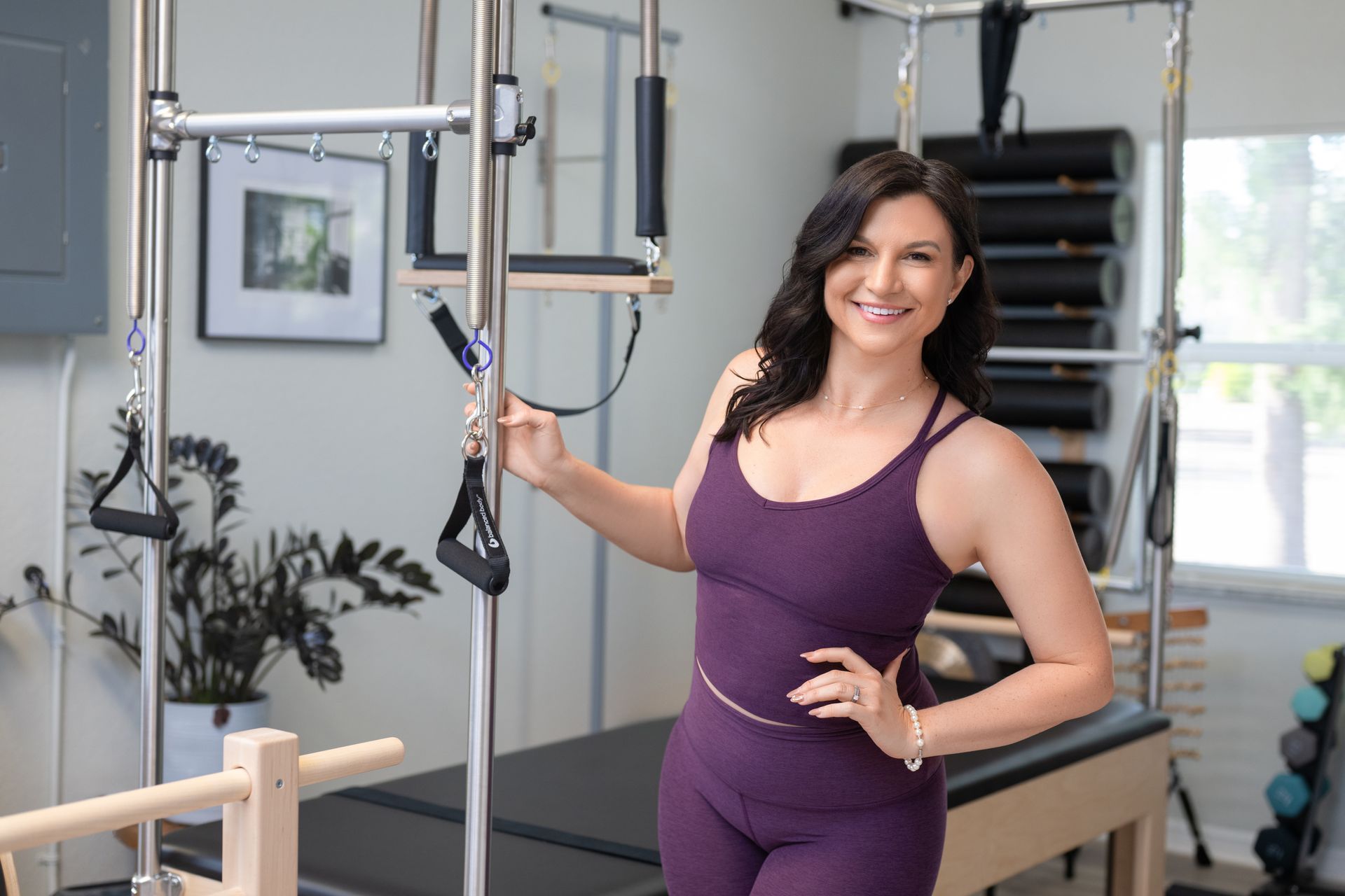 Woman in purple workout clothes holding Pilates straps in a bright studio, smiling
