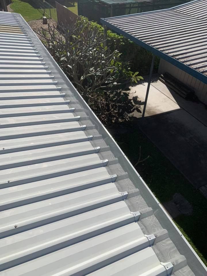 A Man Is Working On A Gutter On The Side Of A Building — Gutter Guard In Forster, NSW