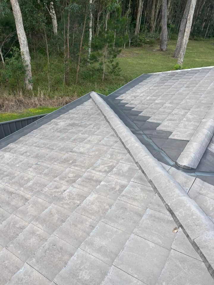 Gray tiled roof with a raised concrete ridge against a backdrop of trees and grass.— Gutter Guard In Wauchope, NSW