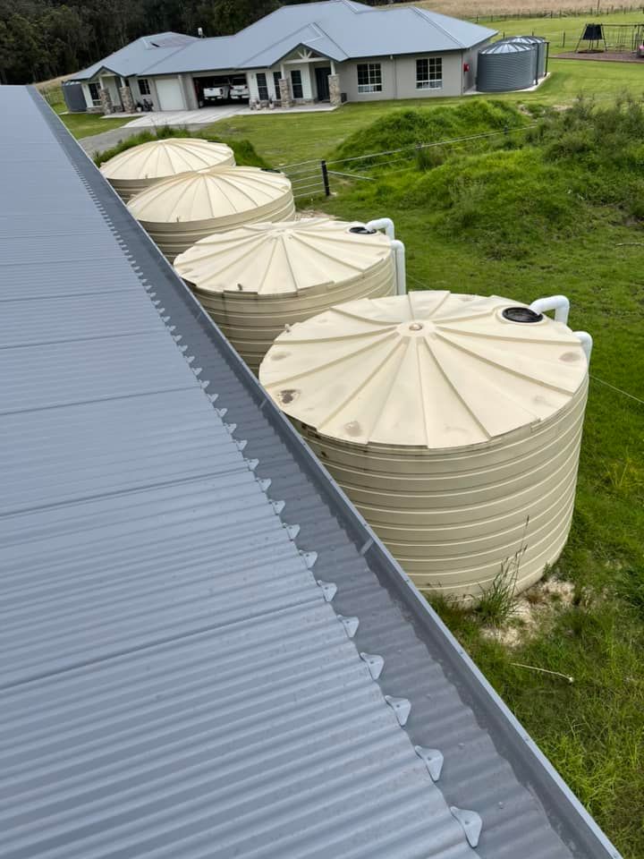 Grey corrugated roof with four beige water tanks next to it, and a house in the background — Gutter Guard In Lake Cathie, NSW