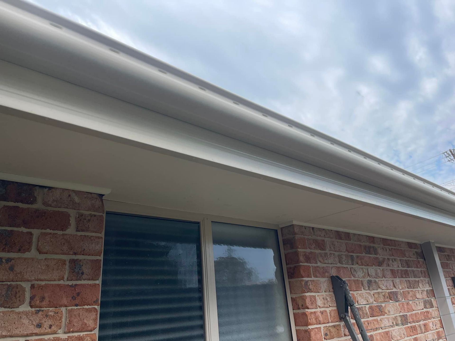 White gutters and trim on a brick house with a cloudy sky in the background.— Gutter Guard In Lake Cathie, NSW