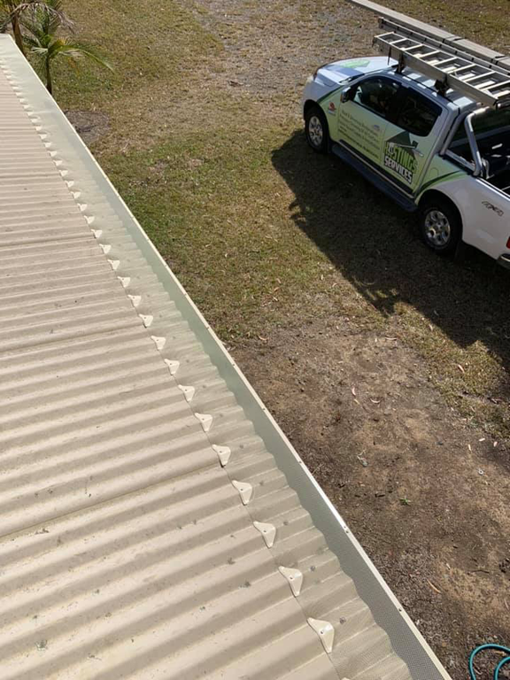 A light-colored corrugated metal roof with triangular roof protectors. A white truck is parked on the grass nearby. — Gutter Guard In Lake Cathie, NSW