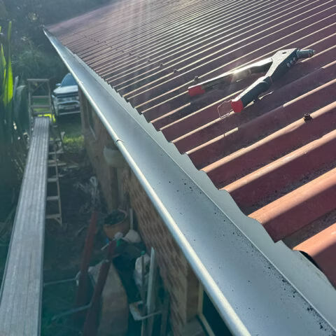 The roof and gutter of a house with a tool on it — Gutter Guard In Lake Cathie, NSW