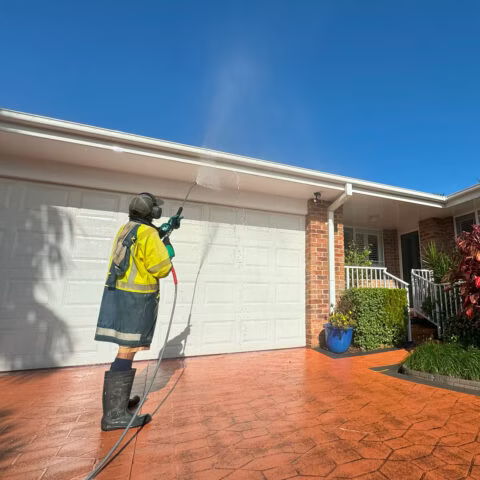 A Man Is Hosing A Gutter On A House — Gutter Guard In Lake Cathie, NSW