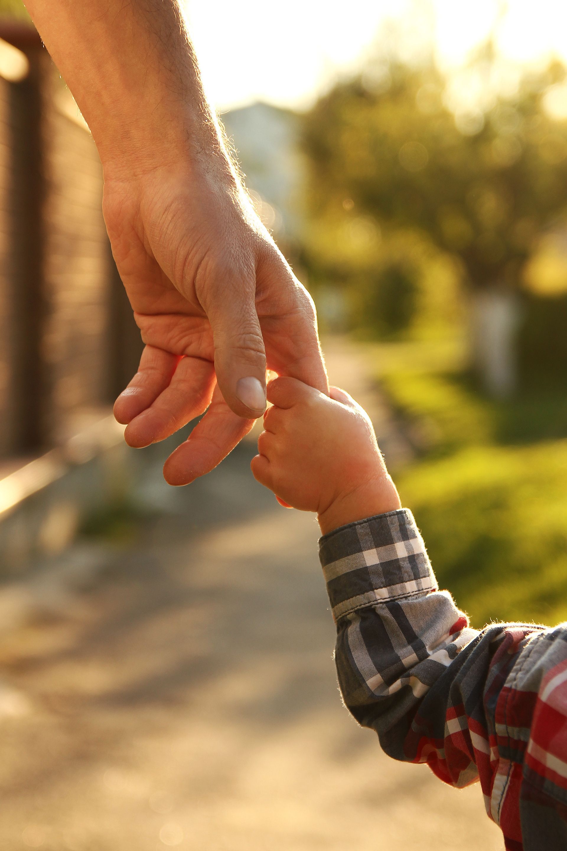 Adult holding a child's hand outdoors in warm sunlight Adult holding a child's hand outdoors in warm sunlight