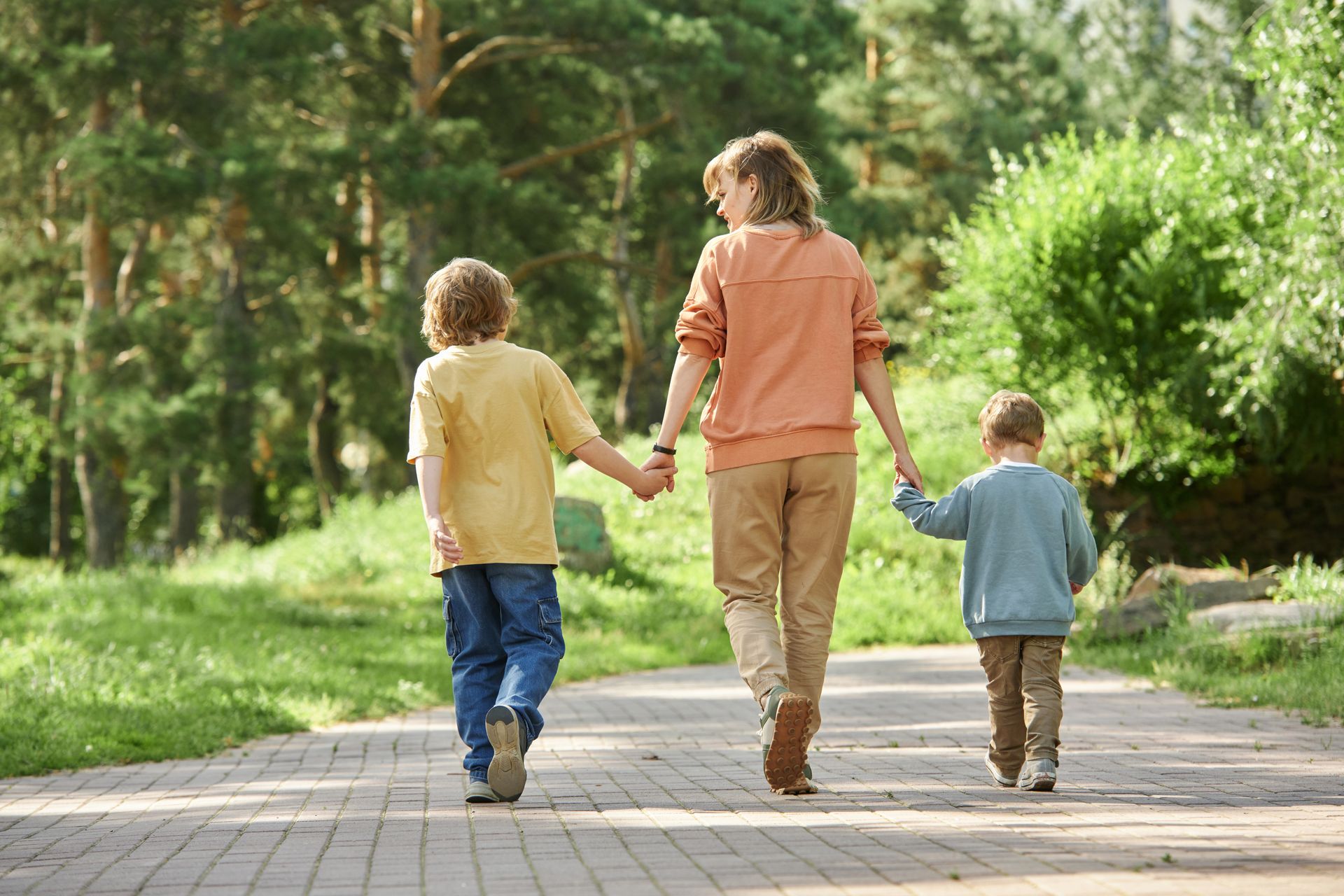 Three children holding hands and walking down a sunlit park path Three children holding hands and walking down a sunlit park path