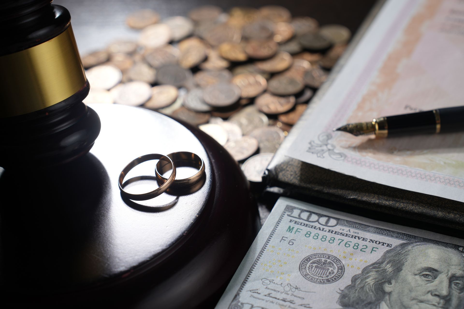 Wedding rings on a judge’s gavel beside cash and a pen. Wedding rings on a judge’s gavel beside cash and a pen.
