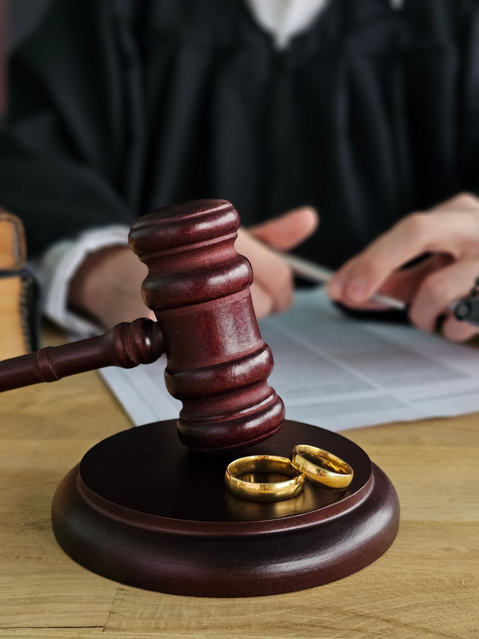 Judge’s gavel beside wedding rings on a desk, with a blurred person in the background Judge’s gavel beside wedding rings on a desk, with a blurred person in the background