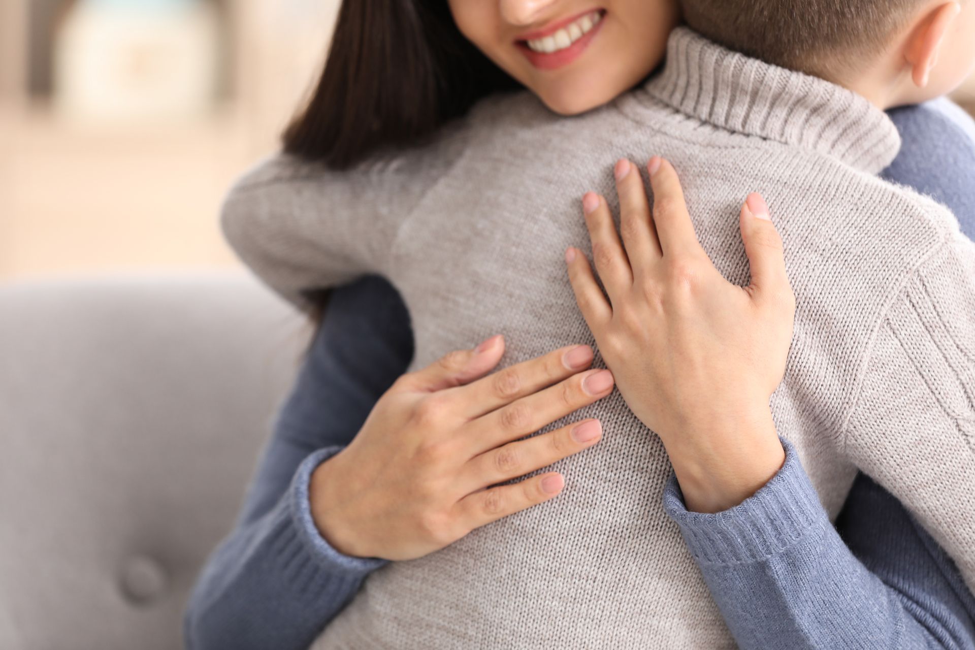 Two people hugging on a couch, with one wearing a gray sweater and the other a blue sweater. Two people hugging on a couch, with one wearing a gray sweater and the other a blue sweater.