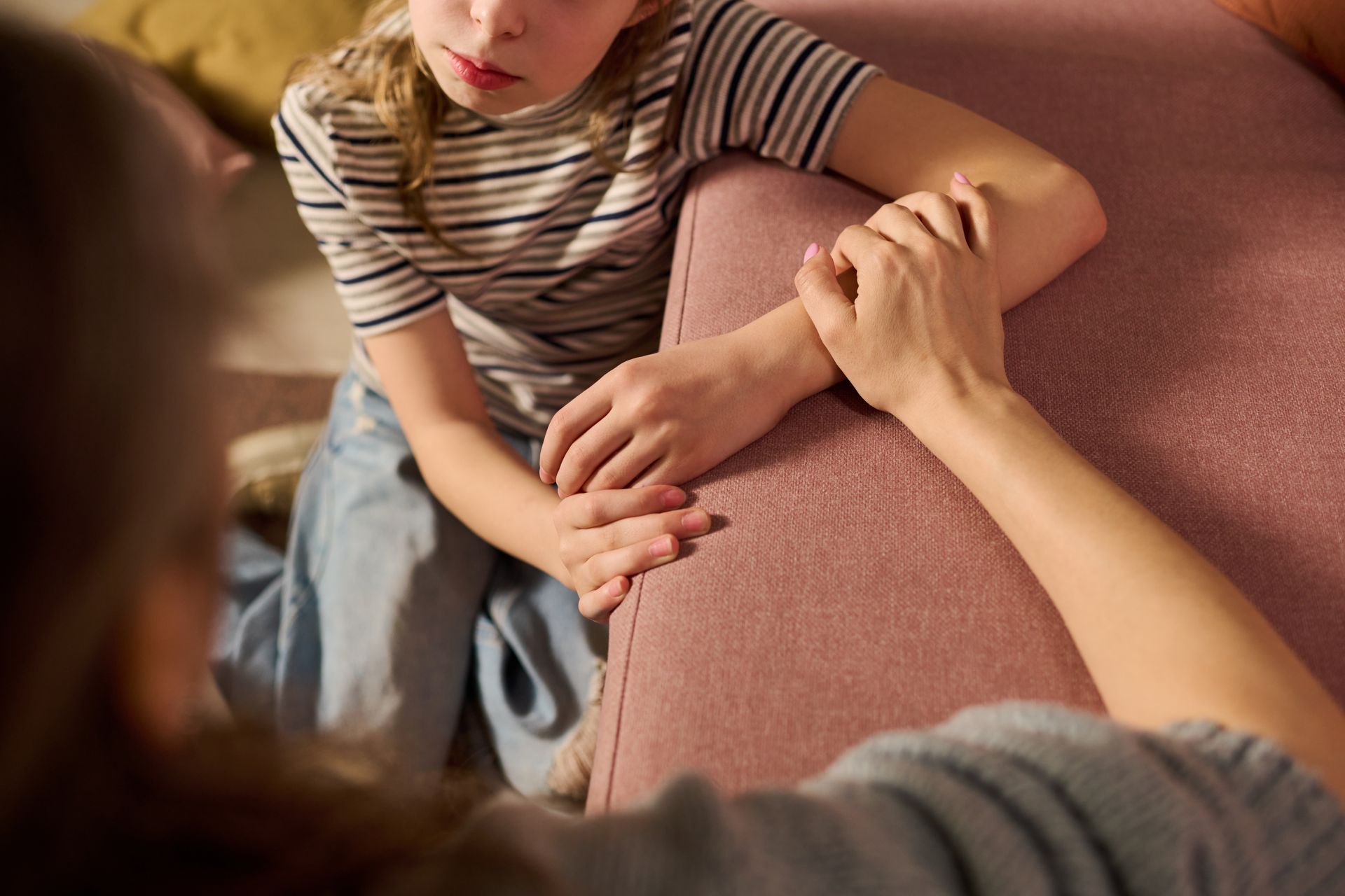 Person sitting on a pink couch, leaning forward with hands clasped, beside another person in the foreground Person sitting on a pink couch, leaning forward with hands clasped, beside another person in the foreground