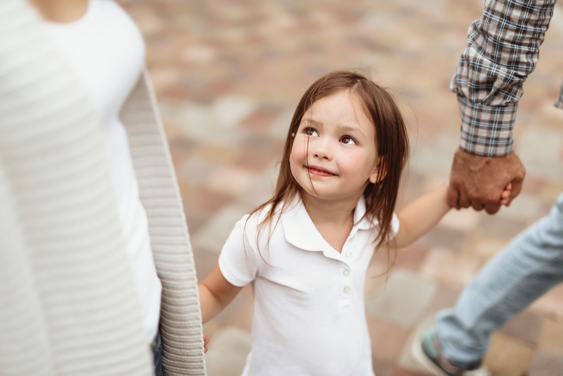 Child holding hands with adults outdoors, looking up and smiling Child holding hands with adults outdoors, looking up and smiling
