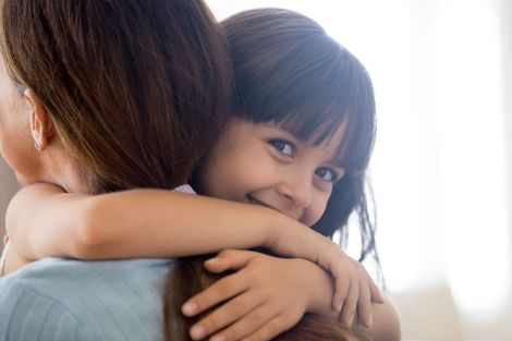 Two children hugging closely indoors, one smiling at the camera Two children hugging closely indoors, one smiling at the camera