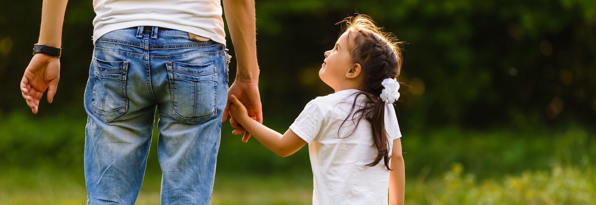 Adult holding hands with a child walking outdoors on a grassy path Adult holding hands with a child walking outdoors on a grassy path