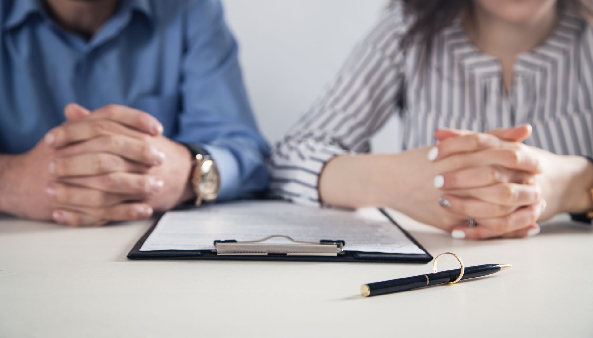 Two people seated at a table with a clipboard and pen in a meeting setting Two people seated at a table with a clipboard and pen in a meeting setting