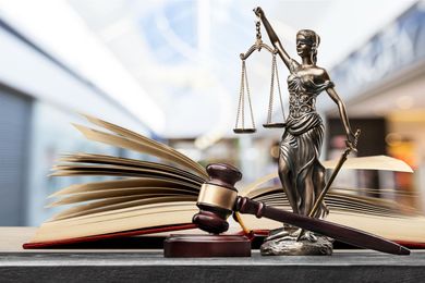Lady Justice statue with scales and gavel beside an open law book on a desk Lady Justice statue with scales and gavel beside an open law book on a desk