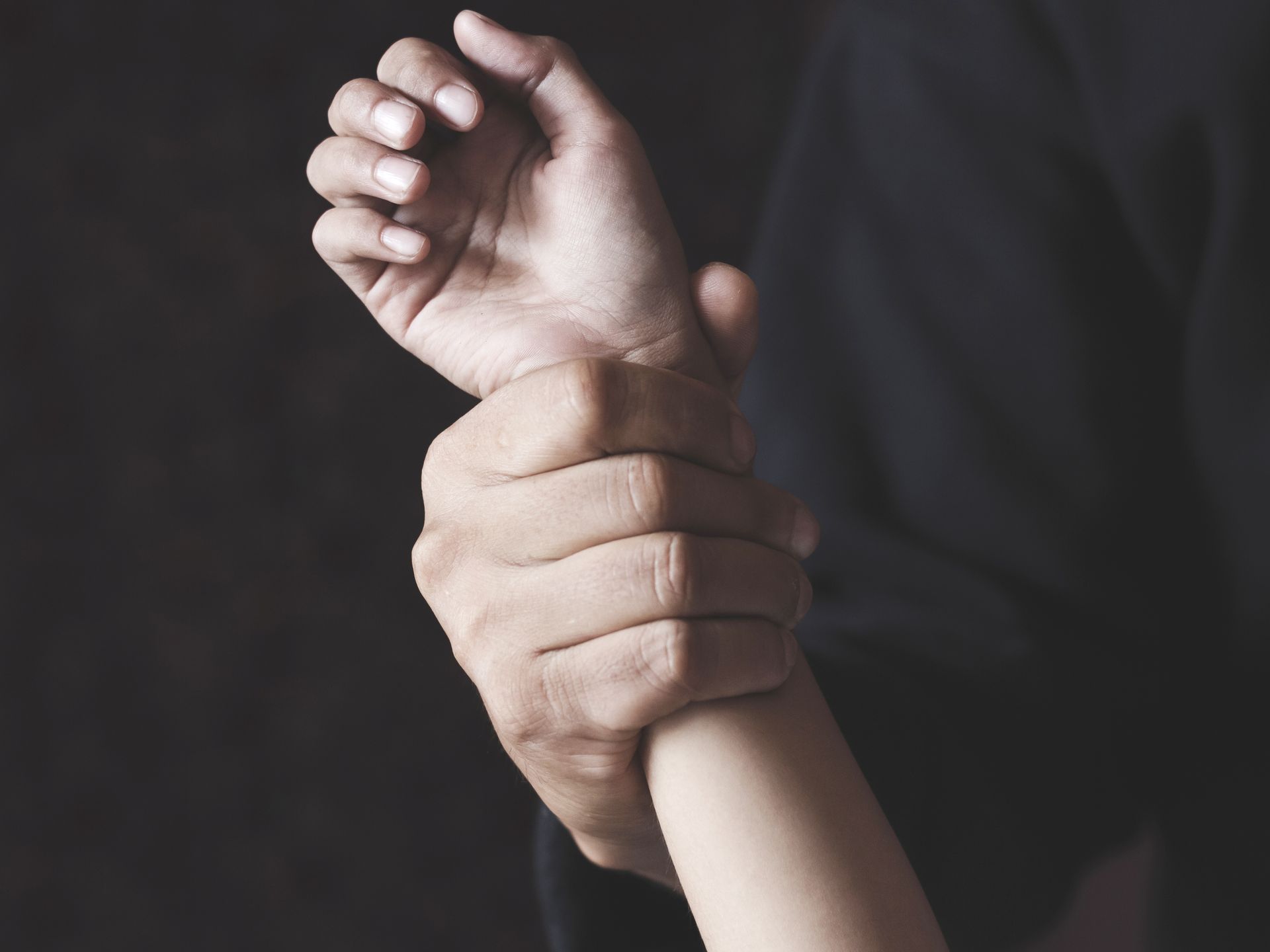 Hand gripping a smaller wrist against a dark background