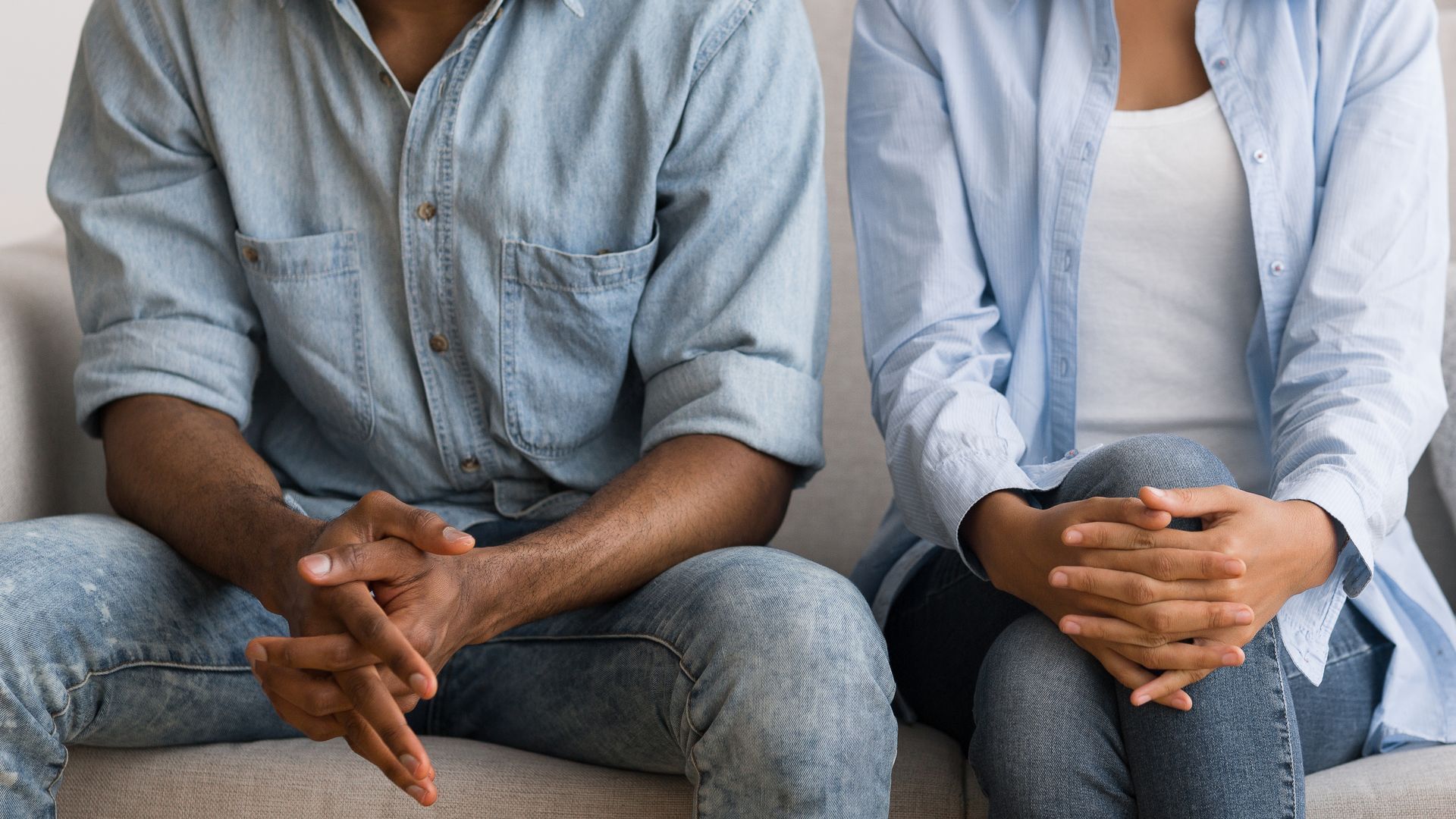 Two people seated side by side, hands clasped, wearing light blue shirts and jeans Two people seated side by side, hands clasped, wearing light blue shirts and jeans