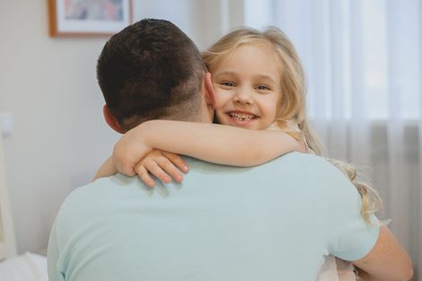 Child hugging an adult from behind in a bright room, smiling warmly Child hugging an adult from behind in a bright room, smiling warmly