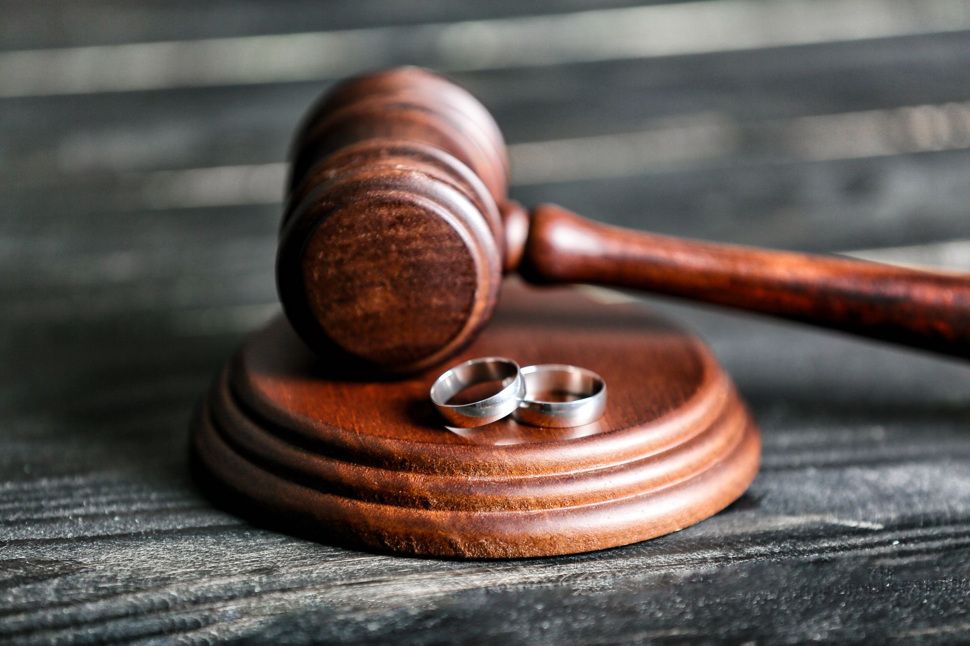 Wooden gavel beside two wedding rings on a dark table Wooden gavel beside two wedding rings on a dark table
