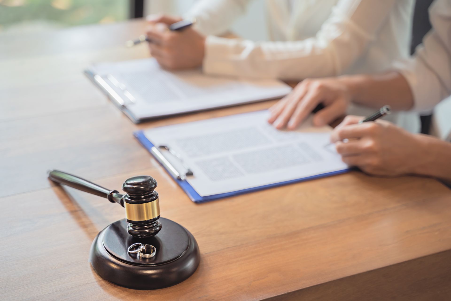 Gavel on desk beside two people reviewing documents and writing on clipboards Gavel on desk beside two people reviewing documents and writing on clipboards