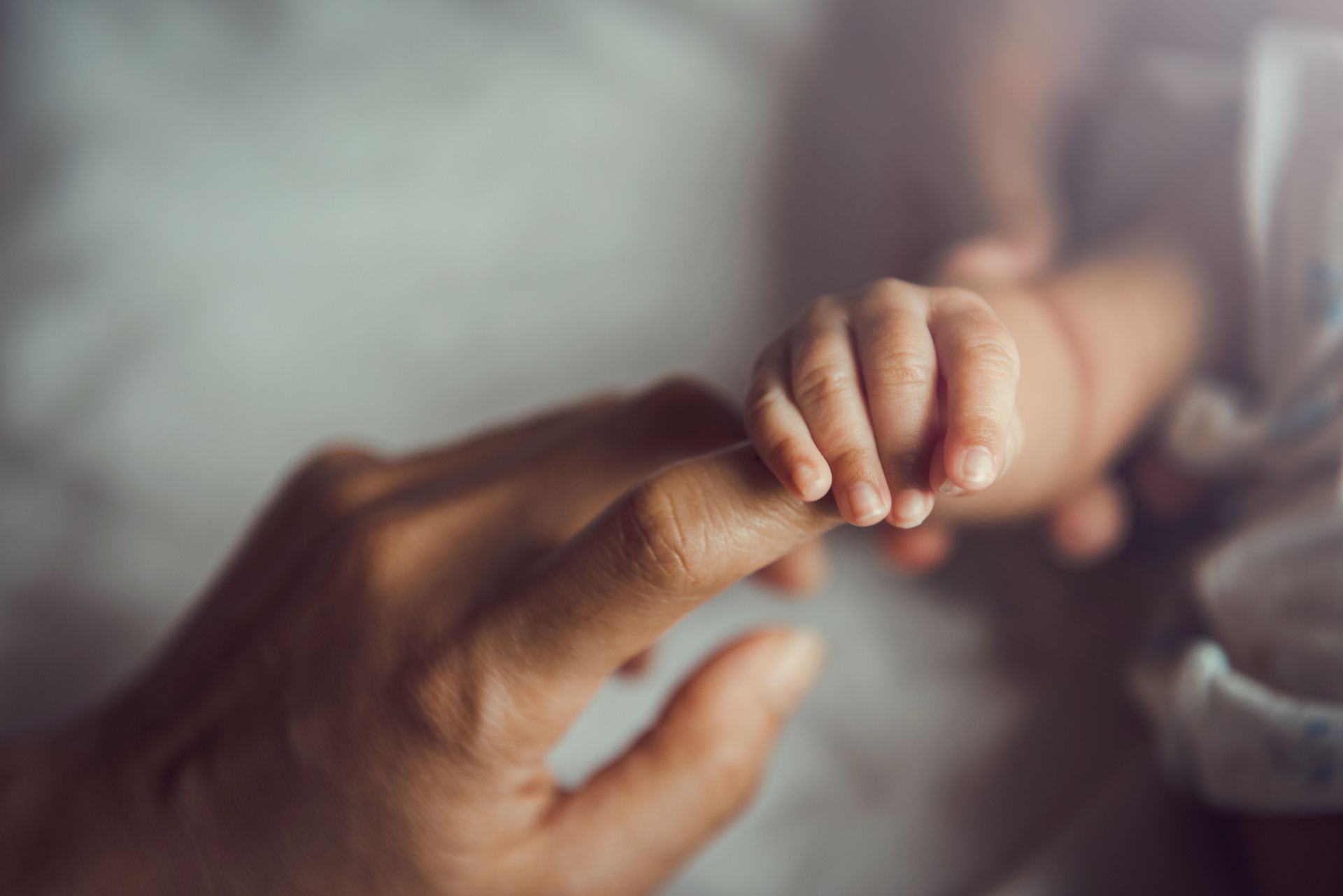 Adult hand gently holding a baby’s tiny fingers in a soft, warm close-up Adult hand gently holding a baby’s tiny fingers in a soft, warm close-up