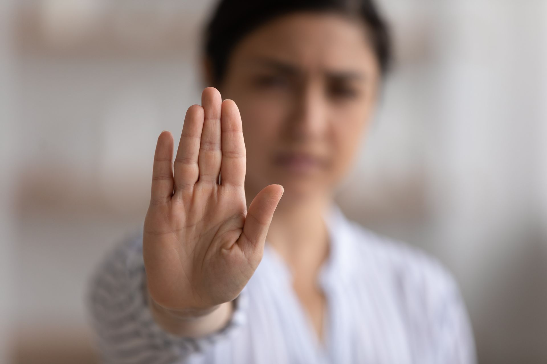 Person holding up a palm in a stop gesture, blurred background indoors